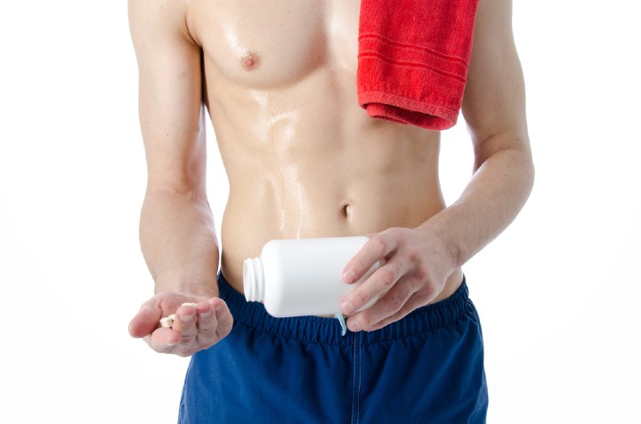 A shirtless, lean young man with a bottle of pills in his hands representing the question: What is the best male fat burner?