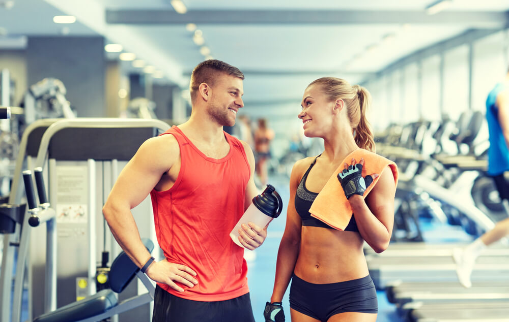 Man and woman looking each other in the gym while holding their protein shakes